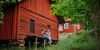 Kaksi naista istuu vanhan punaisen puurakennuksen reunustalla. Ympärlllä vehreitä puita, taustalla toinen punainen puutalo.. Kuvaaja: Julia Kivelä / Visit Finland.